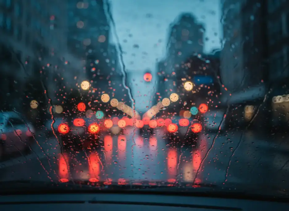 Rain on a windshield at a downtown intersection, brake lights blurred